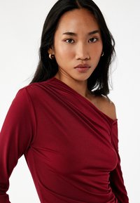 Bordeaux langærmet top i blødt, let materiale med off-shoulder design og draperet detalje langs halsudskæringen og kroppen.