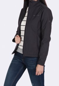 Czarna kurtka typu softshell z wysokim kołnierzem, pełnym zamkiem i dyskretnym logo. Posiada dopasowany krój i jest zestawiona z pasiastą bluzką oraz dżinsami.