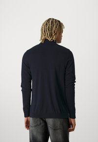 Sweater azul marinho com mangas longas, gola e punhos canelados, textura suave, formato ajustado, usado com jeans cinzentos claros desgastados.