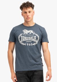 T-shirt de algodón azul oscuro con un gráfico vintage blanco que presenta un león y el texto "The Original Lonsdale London 1960" en el frente.