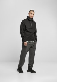Hanorac negru cu fermoar, cu guler înalt, asortat cu pantaloni de trening gri, tapered și adidași negri. Design simplu și materiale confortabile.