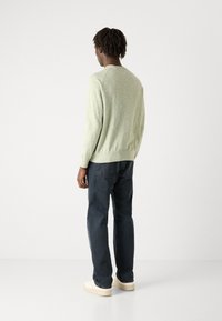 Pulover tricotat de culoare verde deschis, cu mâneci lungi, decolteu rotund și tiv crăpat, asociat cu blugi blue închis și adidași de culoare deschisă.