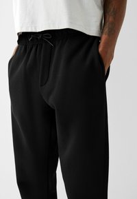 Svarta joggers i mjukt, strukturerat tyg med resårmidja och snörning, sidofickor och en avslappnad passform.