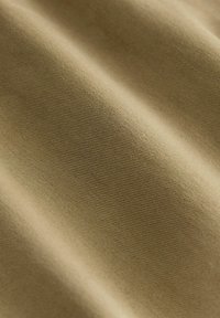 Khaki látka s jemným, textúrovaným povrchom obsahujúcim jemné rebrované vzory, vytvárajúcimi jemné záhyby a kontúry po celej ploche materiálu.