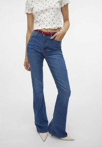 Utvända blå denimjeans med hög midja, med fickor och ett bälte. Bärs med en vit kort topp dekorerad med röda körsbärsmönster.