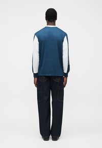 Ναυτικό μπλε μακρυμάνικο πουκάμισο από δίχτυ με λευκά μανίκια και ριμπ μανσέτες, συνδυασμένο με σκούρο τζιν cargo παντελόνι με εμφανή ραφές και τσέπες.