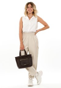 Schwarze strukturierte Handtasche mit einer vorderen Reißverschlusstasche, kombiniert mit beigen Hosen mit elastischem Bund und einem weißen ärmellosen Hemd, getragen mit weißen Sneakers.