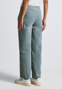 Pantalons vert clair à coupe décontractée avec une finition texturée, taille élastique et poches plaquées, associés à des baskets blanches.