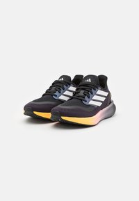 Chaussures de sport noires avec des accents gris et trois rayures blanches, dotées d'une tige texturée, d'une semelle intermédiaire jaune et d'un design léger.