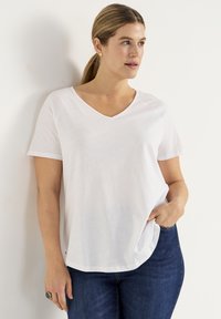 Hvid kortærmet T-shirt med V-hals, lavet af blødt stof. Løs pasform, sideslidser og minimal detail. Parret med blå jeans.