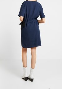 Mörkblå klänning med korta ärmar, lös passform och midja med bälte med en svart satinband. Slät tyg med subtil textur.