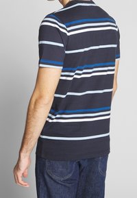 Camisa de manga corta azul marino con rayas horizontales en azul claro, blanco y azul oscuro. Material de algodón, cuello redondo, ajuste holgado.