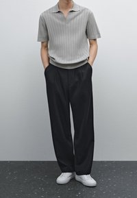 Gray, ribbed polo shirt with a v-neck, paired with loose-fitting black trousers and white sneakers. Simple, modern design. Smooth texture.