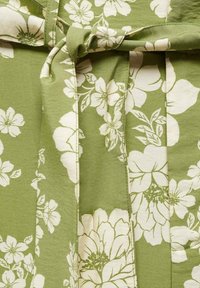 Bloemige jurk van groene stof met witte bloemen. Heeft een geknoopte taille en een zachte textuur. Het ontwerp bevat verschillende bloemgroottes en bladeren.