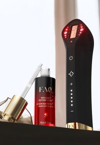 Schwarzes Handgerät mit roten LED-Leuchten, Bildschirm und Bedientasten neben einer Glasdropperflasche mit rotem Peptidserum.