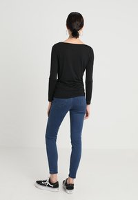 Svart långärmad topp med vid halsringning, tillsammans med blå skinny jeans och svarta sneakers. Enkelt design, figurnära silhuett, stretchigt material.