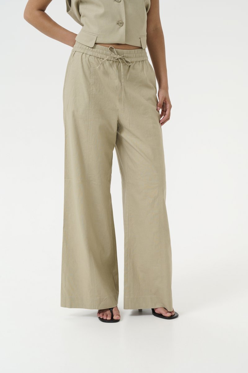 Pantaloni beige chiaro a gamba larga realizzati in un tessuto strutturato, con vita elastica e cordoncino regolabile e tasche laterali.