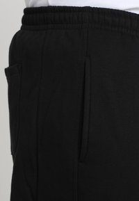 Black joggers made of soft fabric with an elastic waistband, featuring side pockets and a smooth texture. Simple, functional design.