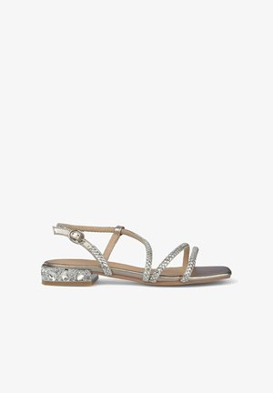 Sandalias plateadas de tiras con tacones planos. Presentan tiras texturizadas y un tacón adornado con piedras preciosas transparentes. Acabado metálico y suave.
