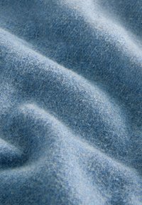 Minkštas, tekstūruotas mėlynas audinys su sulenkta, banguota paviršiumi, kuriame matosi detaliais pluošto audimo ir šešėliavimo efektai.