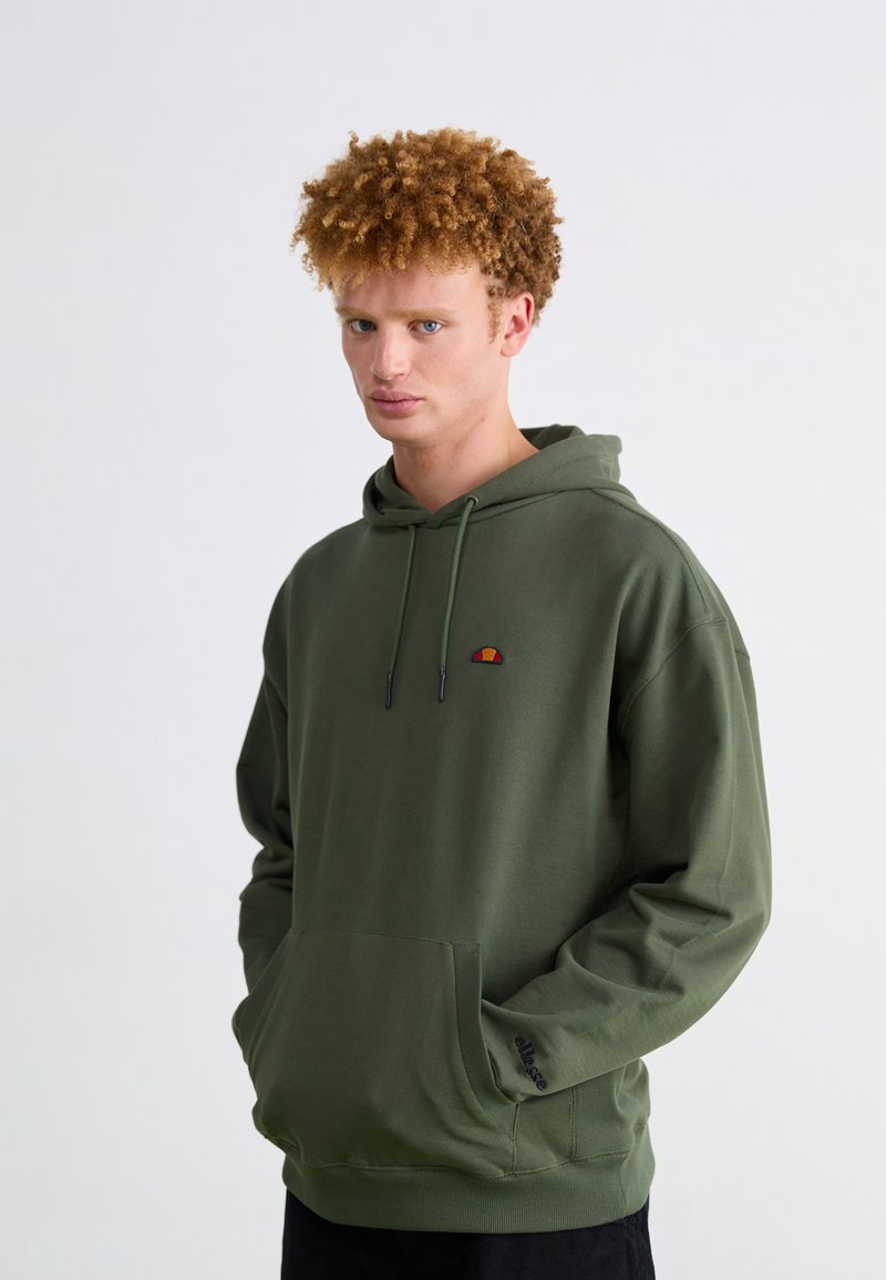 Sudadera verde de tejido suave, con un bolsillo frontal y cordones. Pequeño logotipo de color en el pecho. Ajuste relajado con dobladillo acanalado.