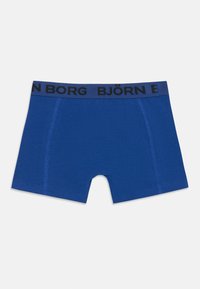 Kék férfi boxeralsó, fekete derékkal, amelyen a márkaneve látható. Lélegző anyagból készült, sima felülettel és varrott szélekkel.
