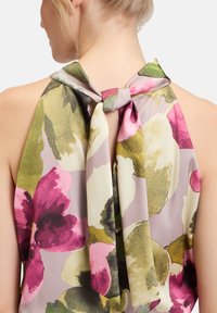 Haut en halter fleuri avec de grands motifs violets et verts, fabriqué dans un tissu léger, avec un détail de nœud au cou.