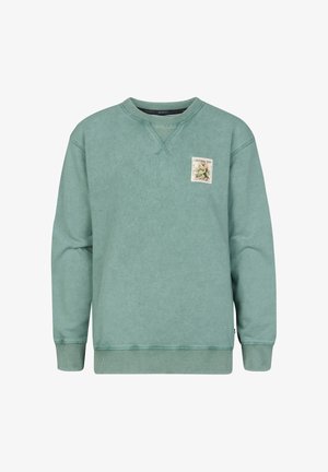 Grüner Baumwollpullover mit rundem Ausschnitt und einem gestickten Emblem. Kombiniert mit grauen Jeans mit weitem Bein und weißen Sneakern.