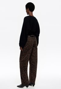 Čierny oversized sveter s dlhými rukávmi v kombinácii s hnedými nohavicami s leopardským vzorom a čiernymi zatvorenými členkovými topánkami na podpätku. Hladká textúra, voľný strih.
