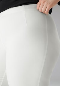 Witte legging met een gladde textuur en een aansluitend ontwerp. Voorzien van een naaddetail langs de zijkant en een hoge taille. Minimalistische stijl.