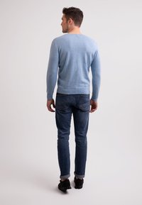 Vaaleansininen neulepaita, jossa on pitkät hihat, pyöreä kaula-aukko ja joustinneulehelma, yhdistettynä tummansinihin farkkuihin ja mustiin kenkiin.