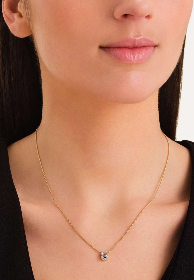 Collier en or avec un pendentif en spirale orné de pierres précieuses transparentes, reposant sur un cou nu, sur un haut noir. Design simple et élégant.