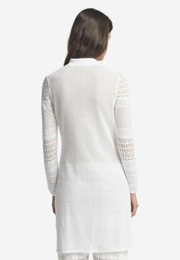 Vit stickad långärmad topp med öppet mönster, med texturerade ärmar och låg rygg. Lätt och andningsbart material.
