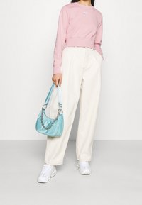 Felpa cropped rosa chiaro, pantaloni crema a vita alta e sneakers bianche. Tiene una borsa azzurro chiaro con un dettaglio in catena argentata.