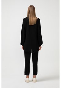 Sort langærmet top med en løs pasform, akkompagneret af sorte smalle bukser. Outfittet har en afslappet silhuet og en subtil tekstur.