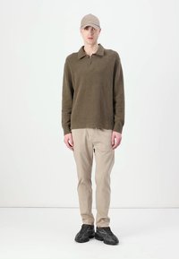 Olivgrüner, strukturierter Pullover mit Kragen und Knopfleiste, kombiniert mit beigen Hosen und schwarzen Sportschuhen. Einfaches, modernes Design.