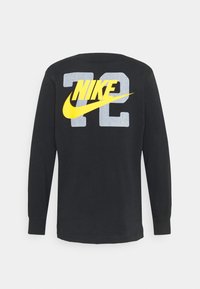 Camisa de manga larga negra con el gran número gris "72" y el logo amarillo de Nike impreso en la parte posterior, exhibida contra un fondo liso.