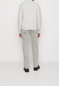 Pull en maille gris clair avec un col montant, associé à un pantalon en denim gris clair. La tenue présente une coupe décontractée et des poignets côtelés.