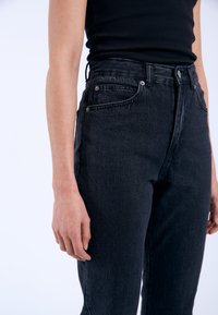 Högmidjade svarta jeans i denim, med fem fickor, metallfästen och en smal passform som avsmalnar ner längs benet för en modern silhuett.