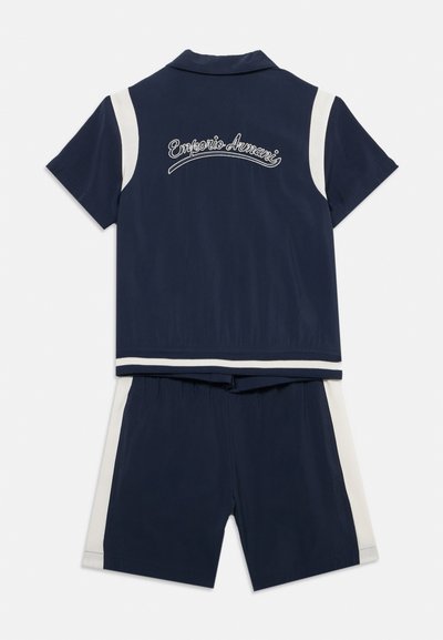 Ναυτικό μπλε σύνολο δύο τεμαχίων με κοντά μανίκια και σορτς, λευκές πλευρικές ρίγες και κεντημένο "Emporio Armani" στην περιοχή του πίσω γιακά.
