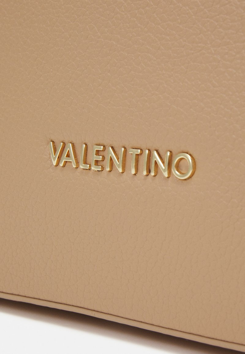 Borsa a mano in pelle beige con superficie testurizzata e logo "VALENTINO" in oro embossato in un font elegante e moderno.