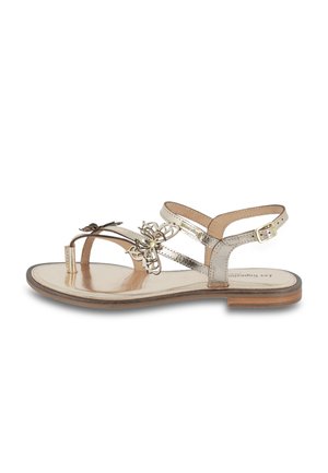Sandal in metallo dorato con suola piatta, caratterizzato da un accento floreale, due cinturini alla caviglia e un design minimalista. Finitura in pelle liscia.