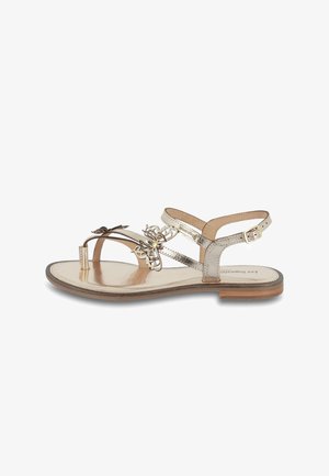 Metallic gold sandal with a flat sole, featuring a floral accent, two ankle straps, and a minimalist design. Smooth leather finish.