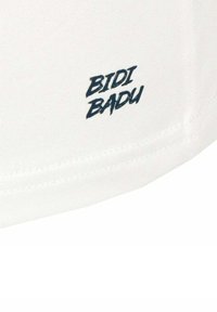 Camiseta blanca con un diseño ajustado, que presenta un logo en azul oscuro "BIDI BADU" en el lado inferior. Tejido suave con una textura sutil.