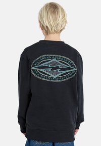Svart hettegenser med ribbestrikkede mansjetter og nederkant, med et stort grafisk trykk i turkis og grått på baksiden med teksten "Billabong Boardshorts".