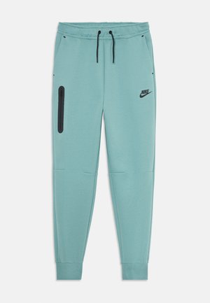 Pantaloni da tuta Nike di un azzurro chiaro con cordini neri, polsini a coste, tasche laterali e tasche sulla coscia con zip, e logo Nike nero sulla coscia destra.