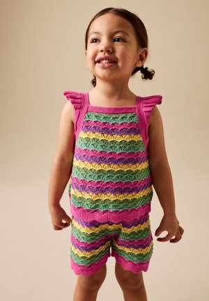 Ung pige, der smiler og bærer en farverig strikket ærmeløs top og matchende shorts med pink, grønne, gule og lilla striber.