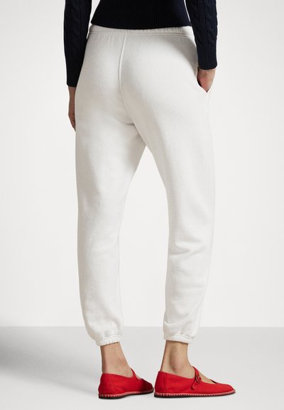 Fehér melegítőnadrág rugalmas mandzsettákkal és oldalzsebekkel, puha anyagból készült, piros, lekerekített kialakítású, könnyen felhúzható cipőkkel párosítva.