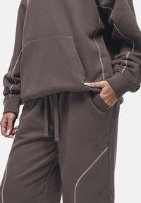 Bruine katoen sweatshirt met een voorzak en decoratieve witte stiksels, gecombineerd met bijpassende joggingsbroek met een elastische tailleband en zakken.