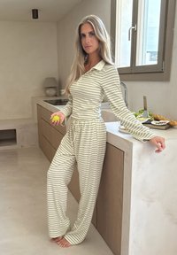 Conjunto de loungewear a rayas en verde claro y blanco, que presenta una blusa con cuello y pantalones con cordón, fabricado en tejido suave y con un corte relajado.
